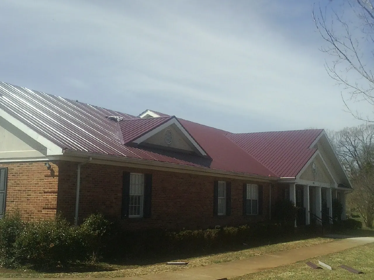 Red metal roof with gabled entries on a long brick building, from a Hail Damage Roof Repair job in Westport